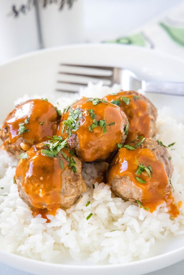 Porcupine meatballs served over a bed of white rice in a bowl with a fork.