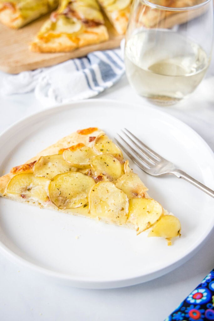slice of potato pizza on a white plate with a fork