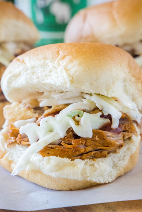 Close up of a pulled pork slider with coleslaw, with two more in the background.