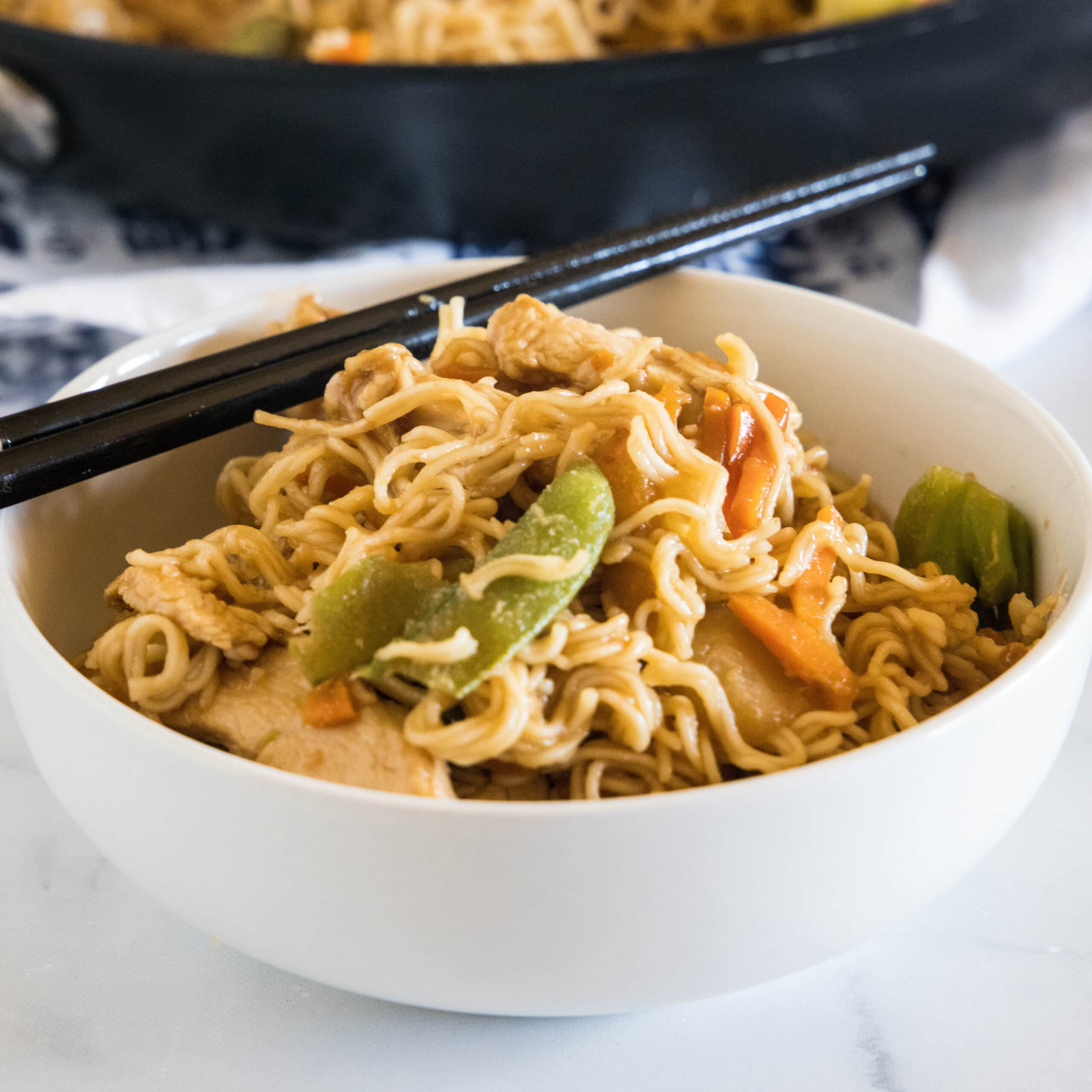 Ramen stir fry in a white bowl with a set of chopsticks resting on the rim of the bowl.