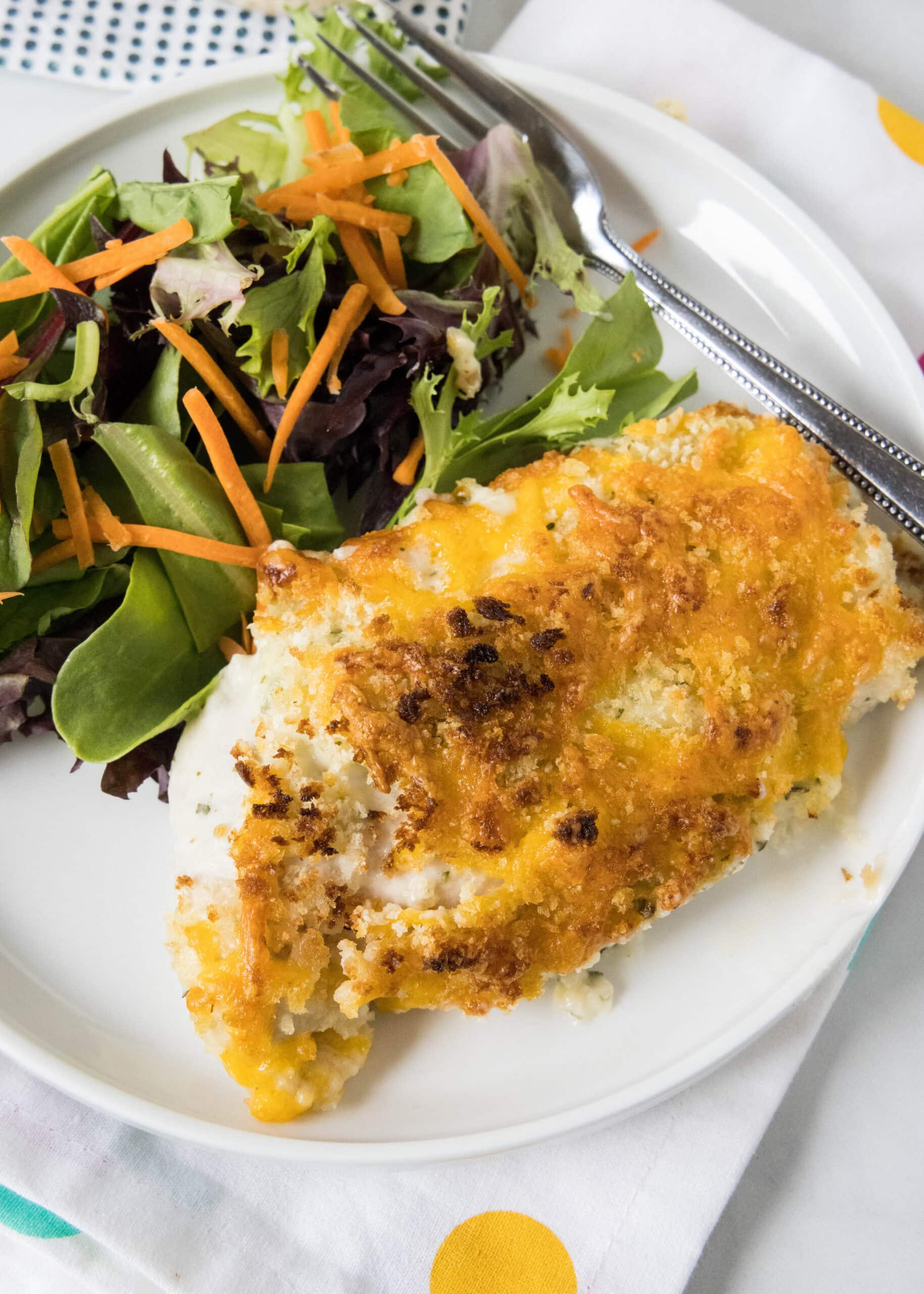 Baked ranch chicken served with a side of salad on a white plate.