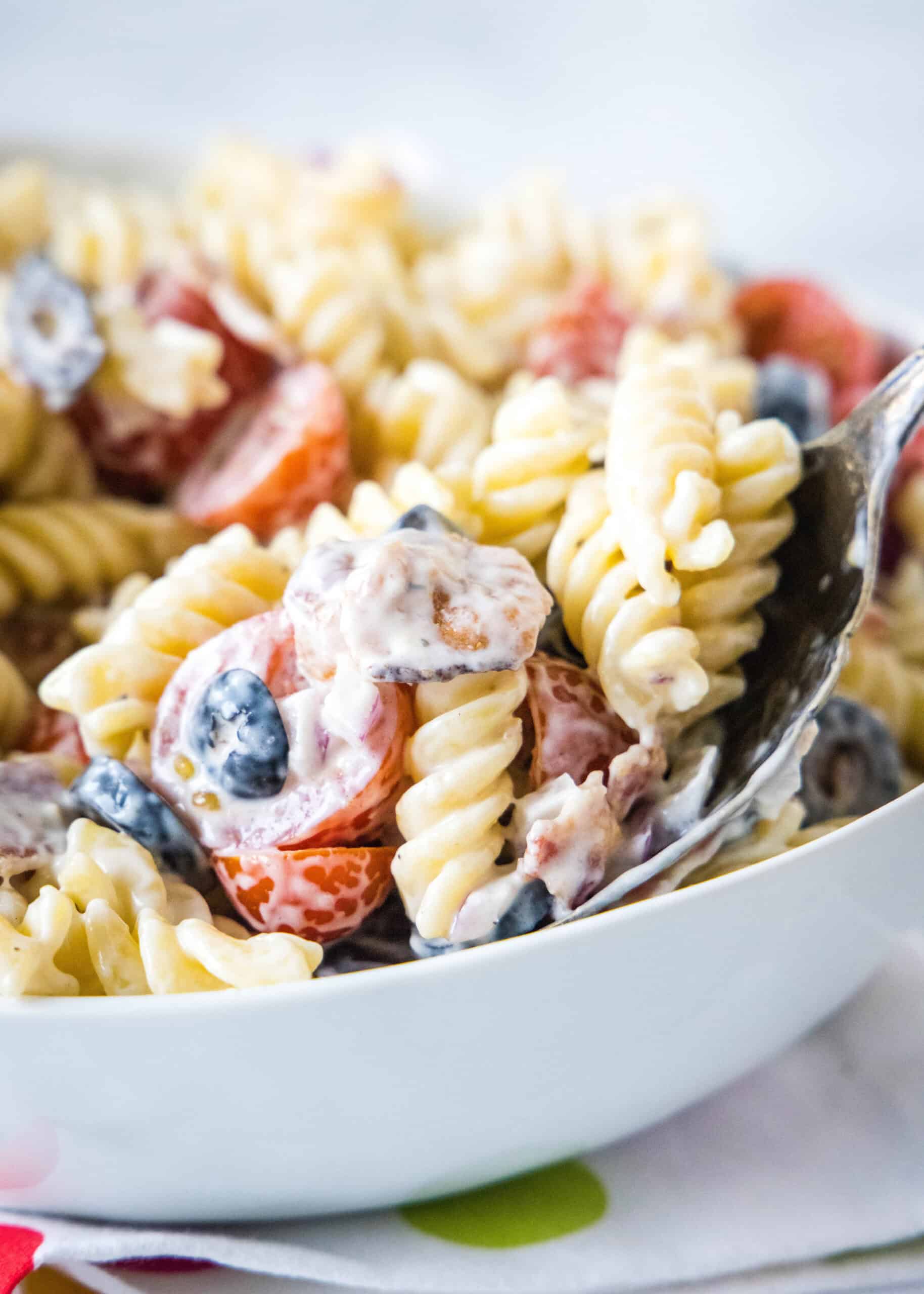 A large serving spoon scooping ranch pasta salad from a white bowl.