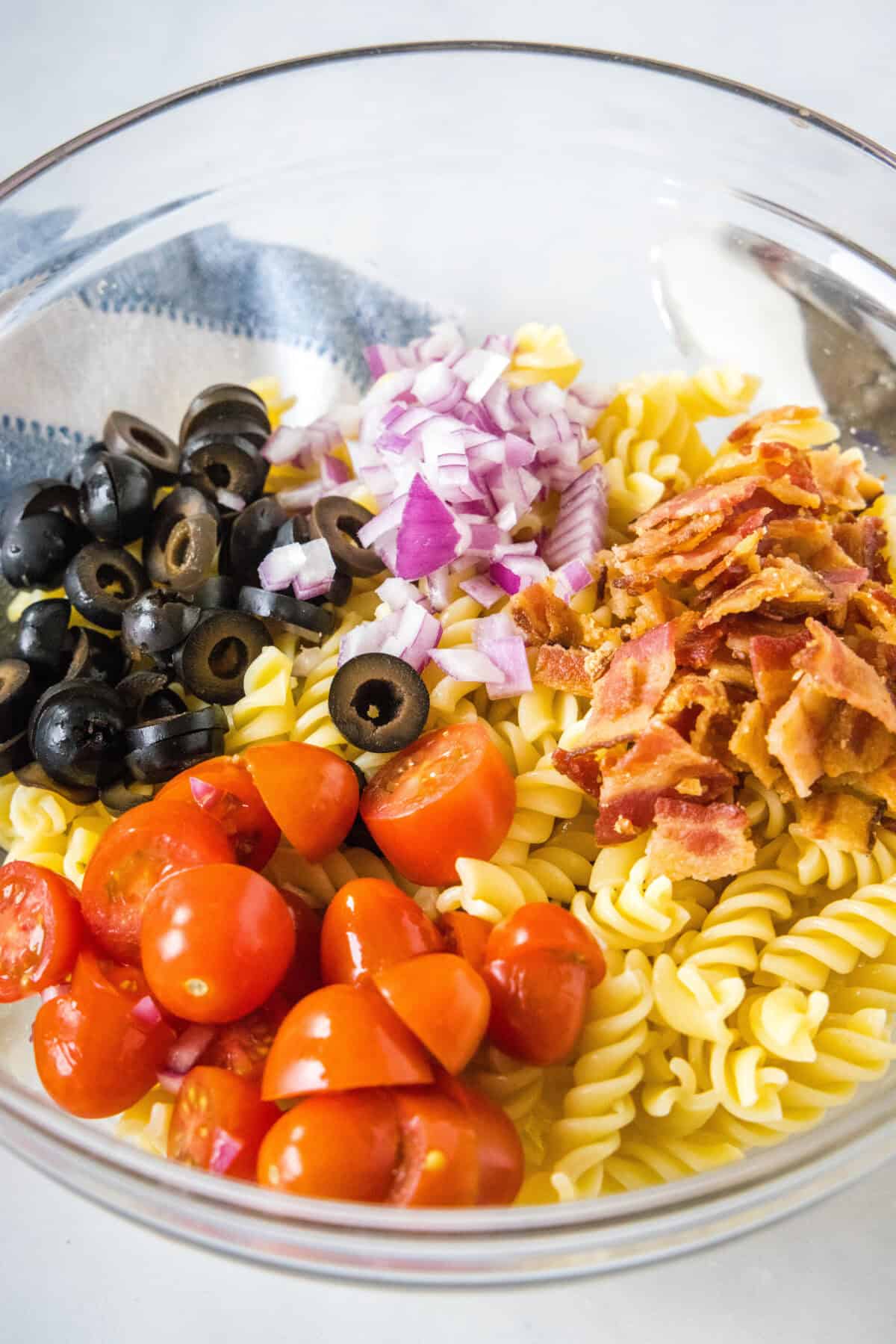 Ranch pasta salad ingredients combined in a glass bowl.