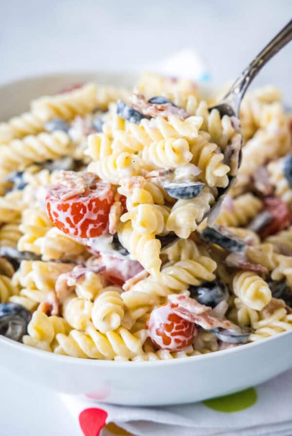 A large serving spoon scooping ranch pasta salad from a white bowl.
