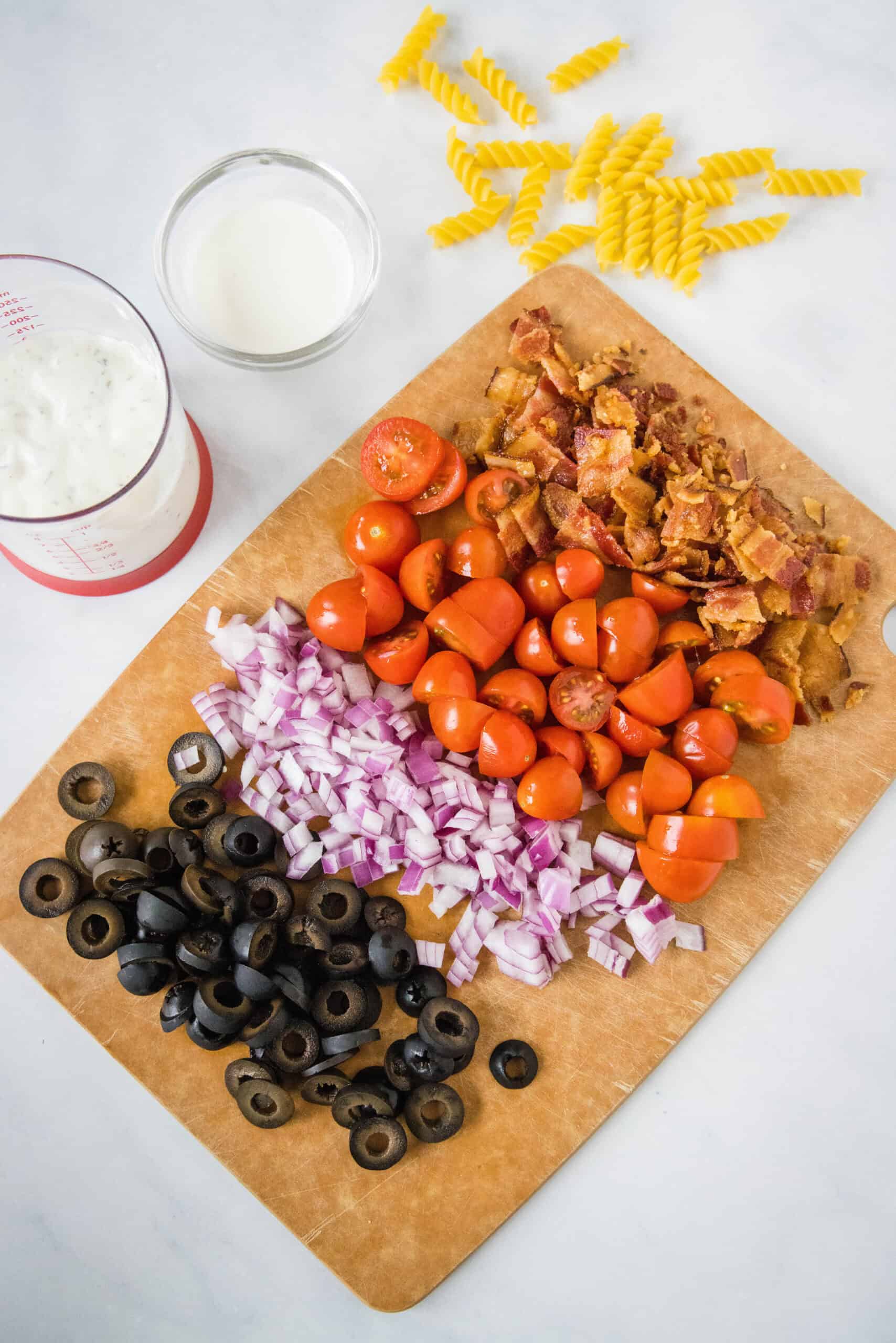 Ranch pasta salad ingredients prepared on a wooden cutting board.