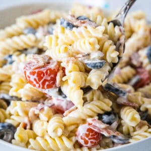 A large serving spoon scooping ranch pasta salad from a white bowl.