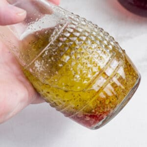 A hand holding up a carafe of red wine vinaigrette.