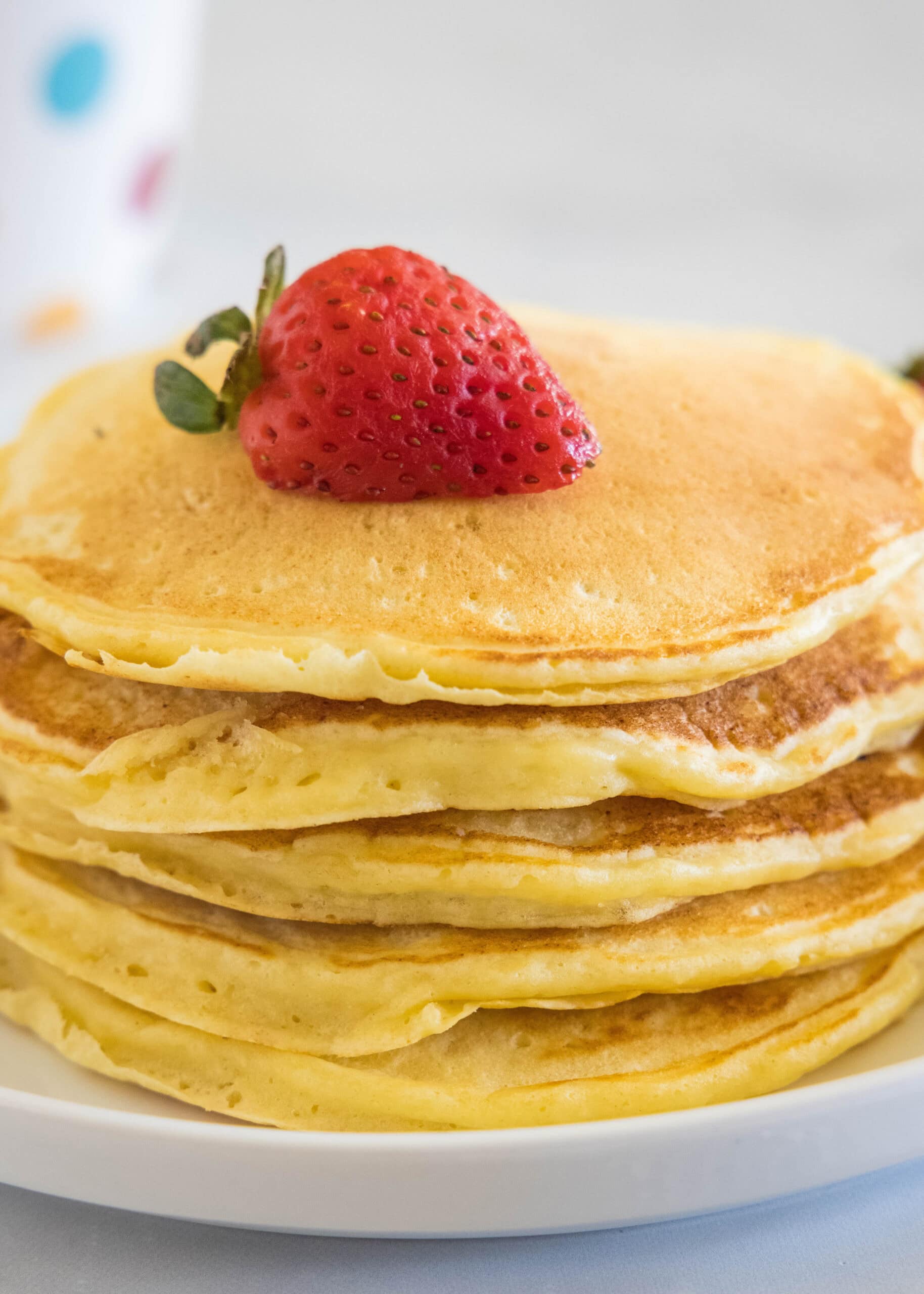 A stack of ricotta pancakes topped with a strawberry a plate.