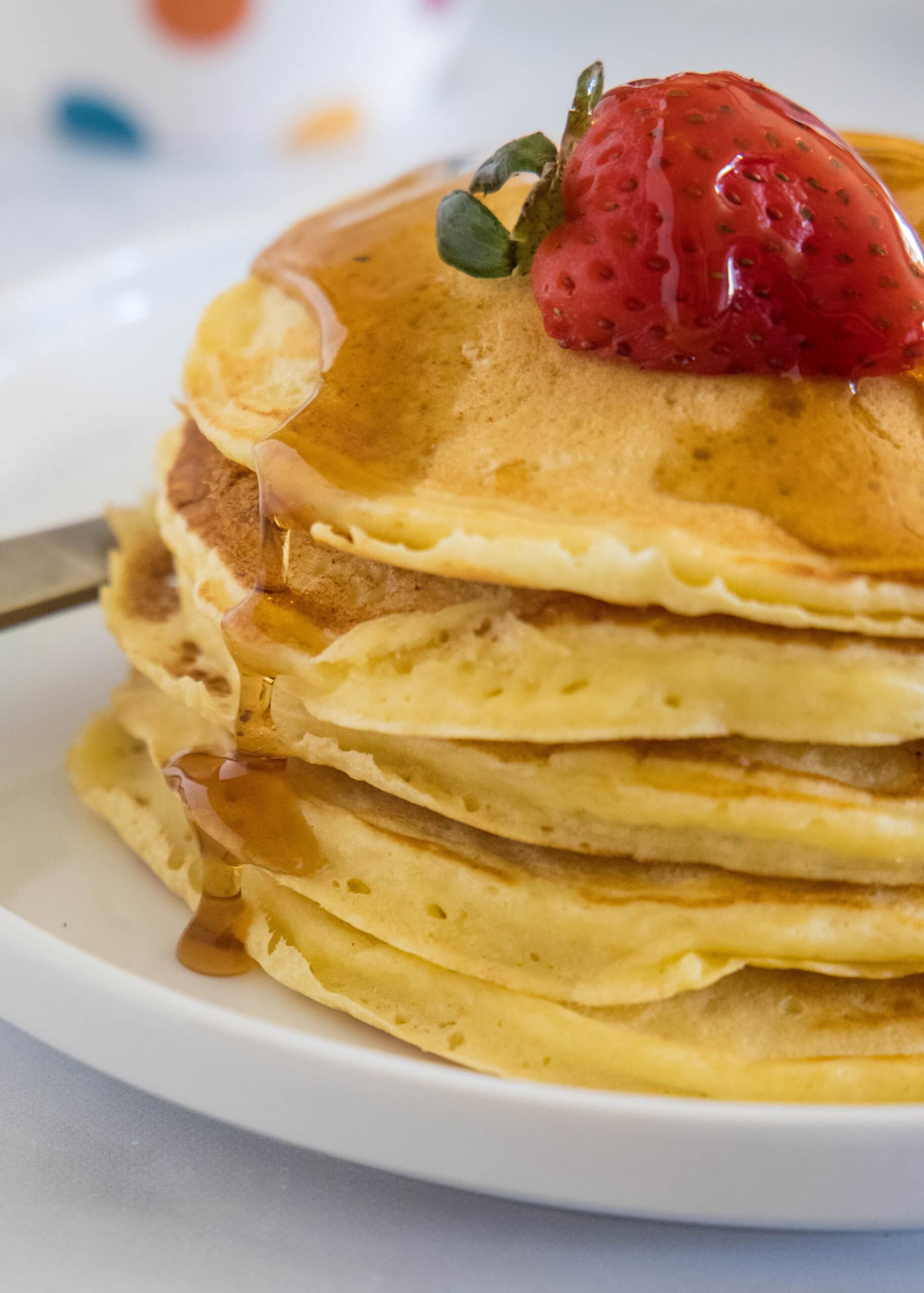 A stack of ricotta pancakes topped with a strawberry and maple syrup on a plate.
