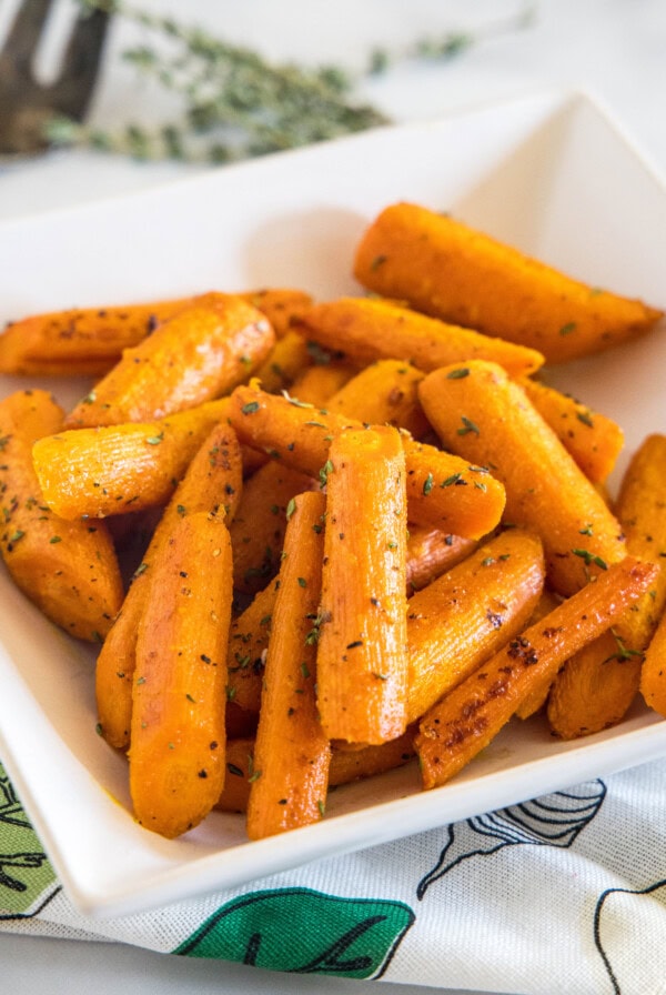 Seasoned roasted carrots in a square white bowl.