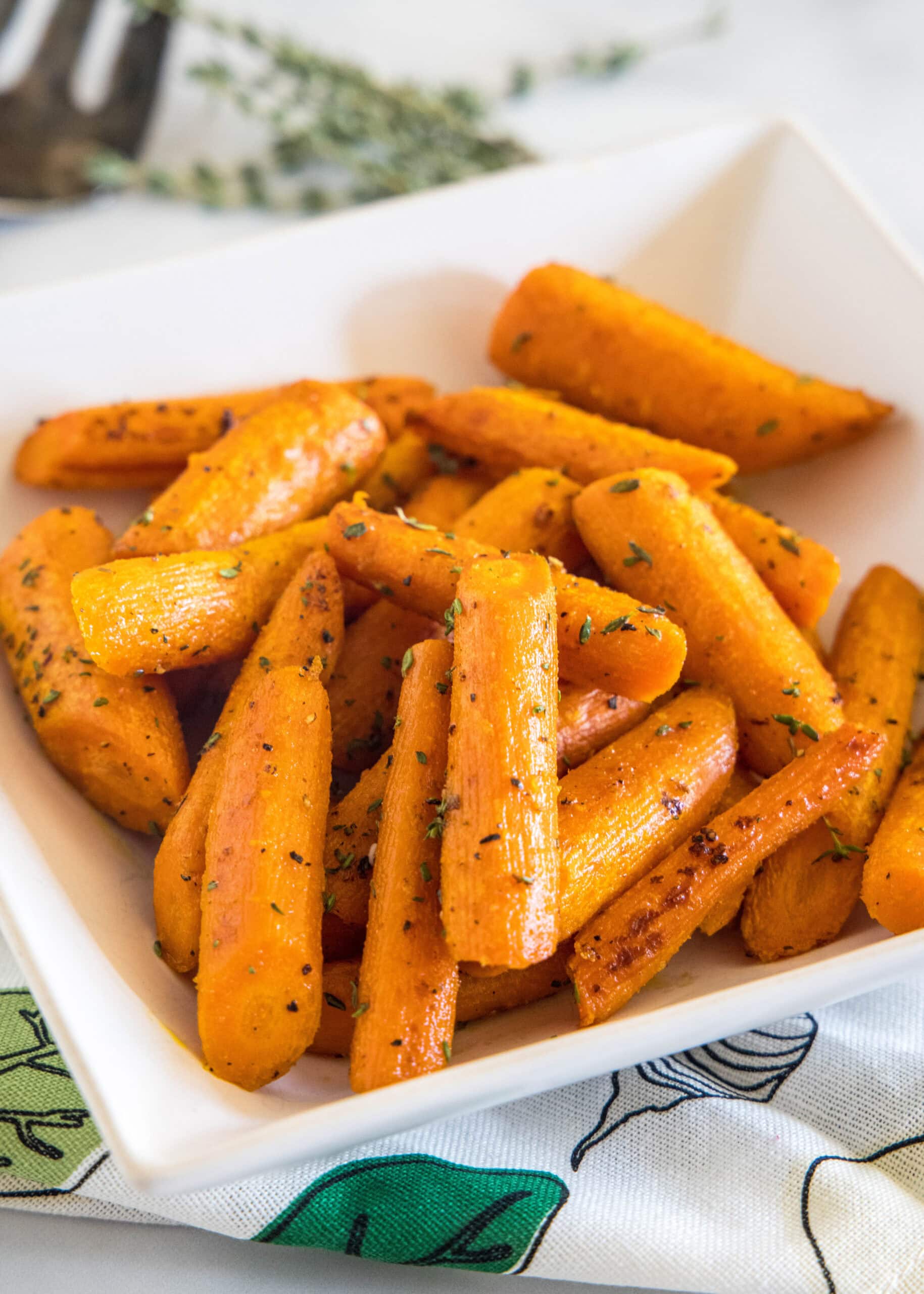 These tender oven roasted carrots come out crispy, caramelized, and full of flavor. They're the perfect easy side dish for any occasion! Seasoned roasted carrots in a square white bowl.