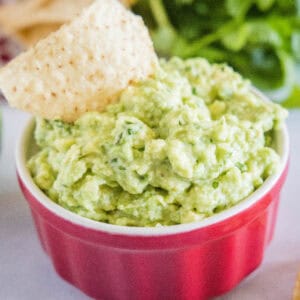 cropped close up roasted garlic guacamole in a bowl with a tortilla chip