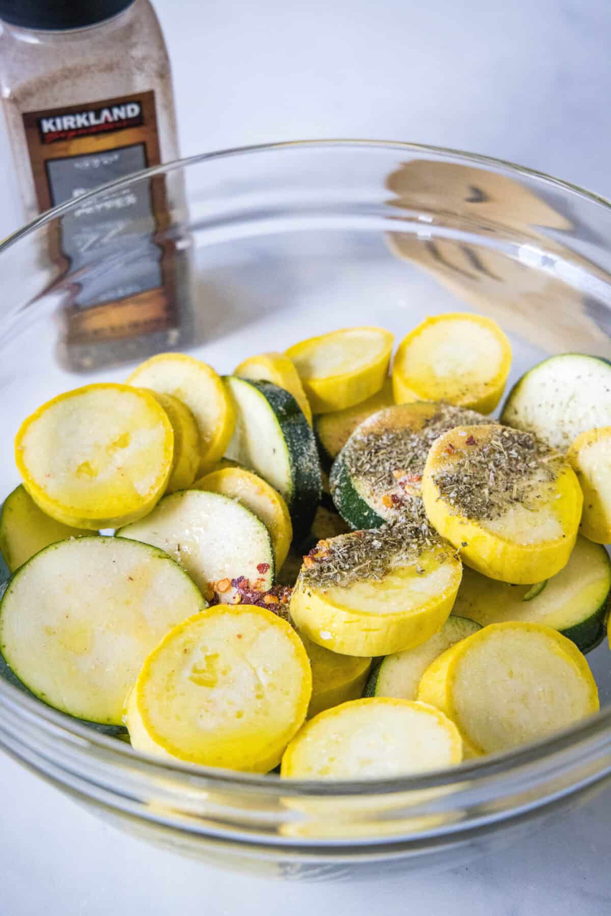 Seasonings added to sliced zucchini and squash in a glass bowll.