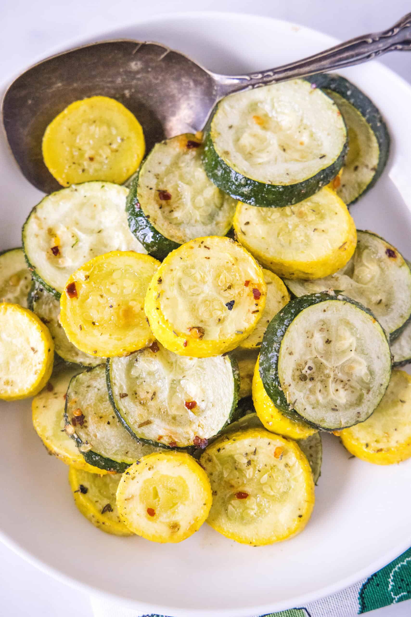 Overhead view of roasted zucchini and squash in a bowl with a serving spoon.
