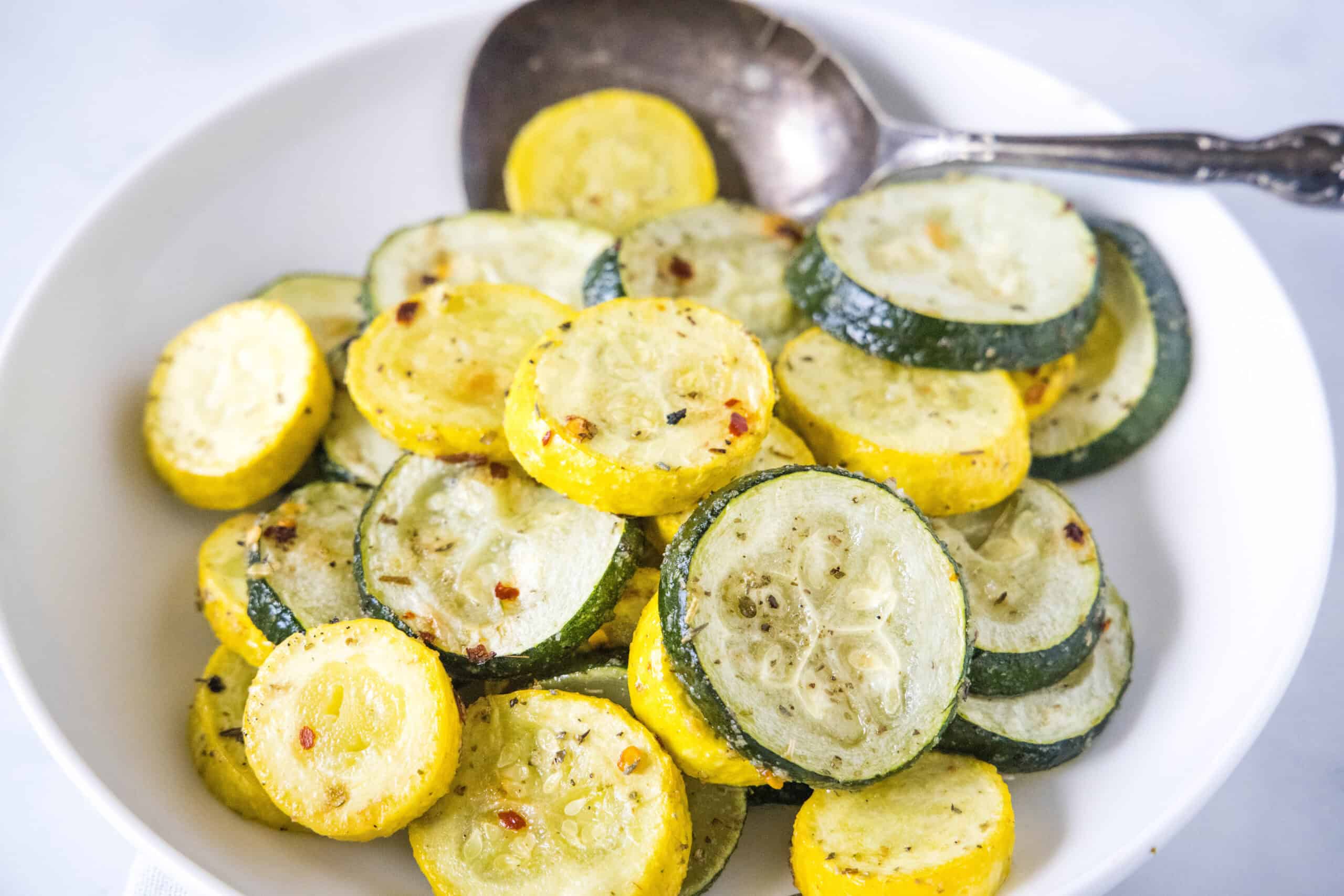 Roasted zucchini and squash in a bowl with a serving spoon.
