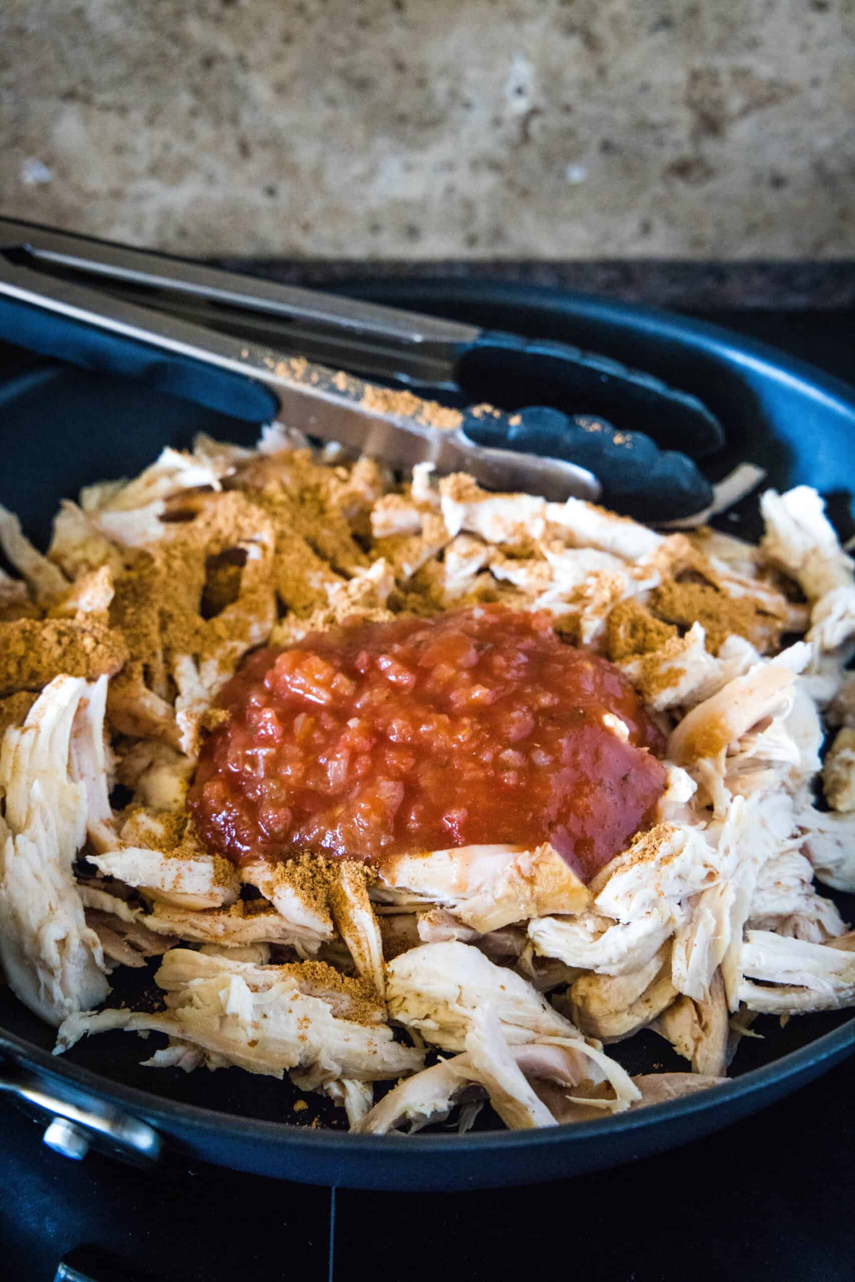 Seasonings and salsa added to shredded rotisserie chicken in a skillet.