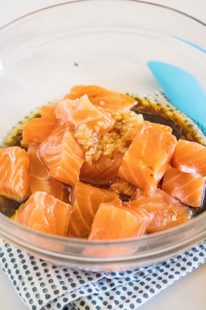 Salmon pieces added to marinade in a glass bowl.