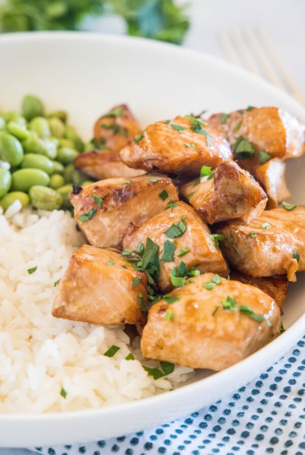 Salmon bites served with rice and edamame beans in a white bowl.
