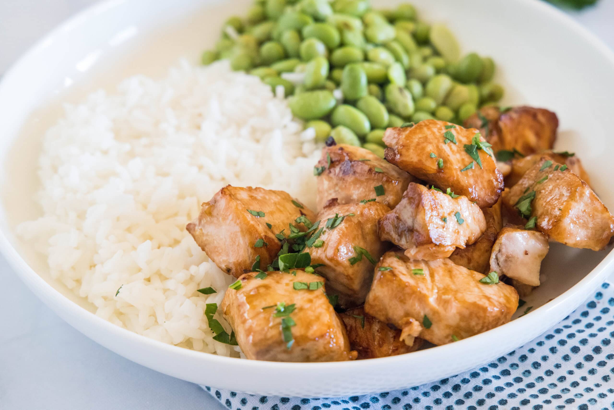 Salmon bites served with rice and edamame beans in a white bowl.