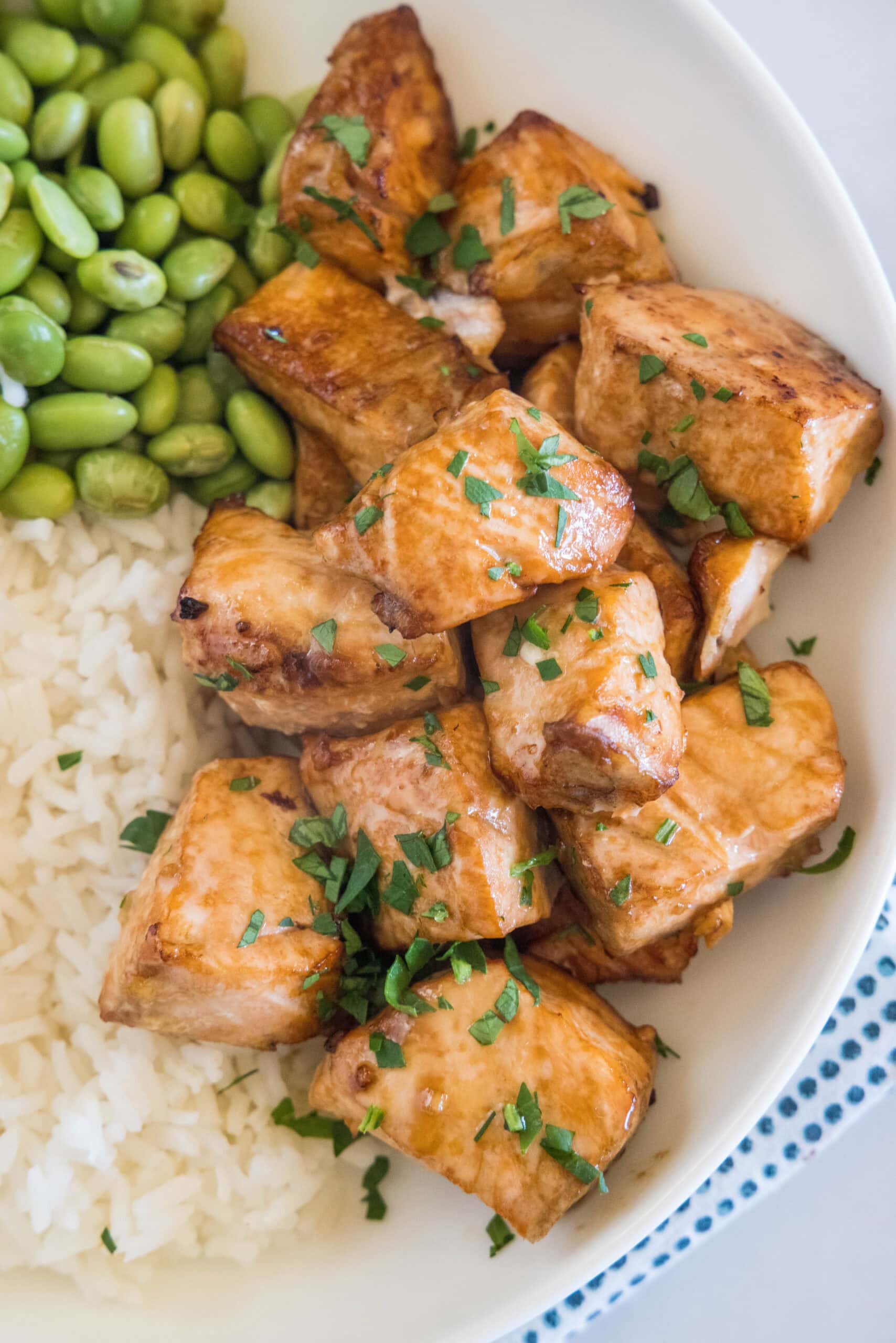 Salmon bites served with rice and edamame beans in a white bowl.