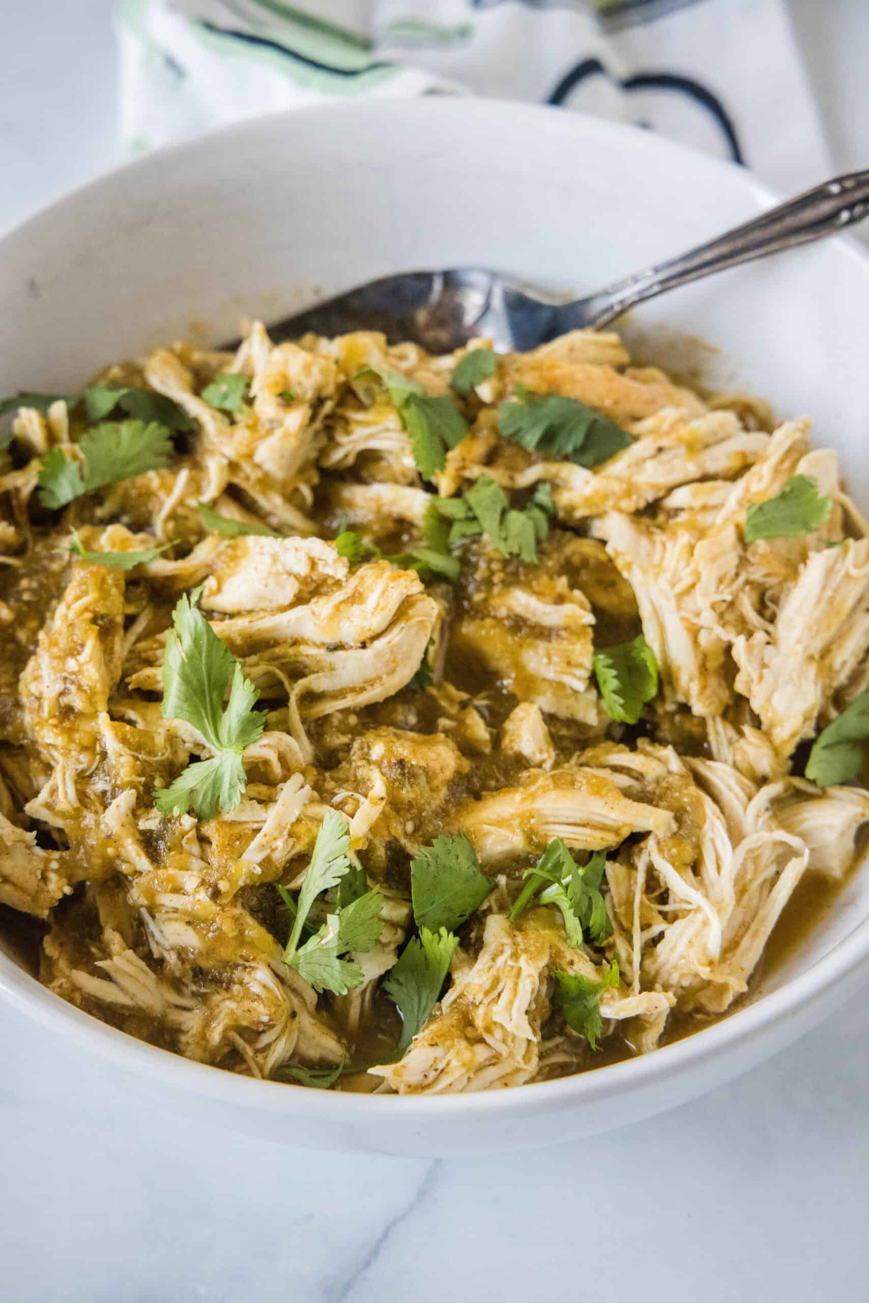 Shredded salsa verde chicken in a white bowl with a spoon for serving.