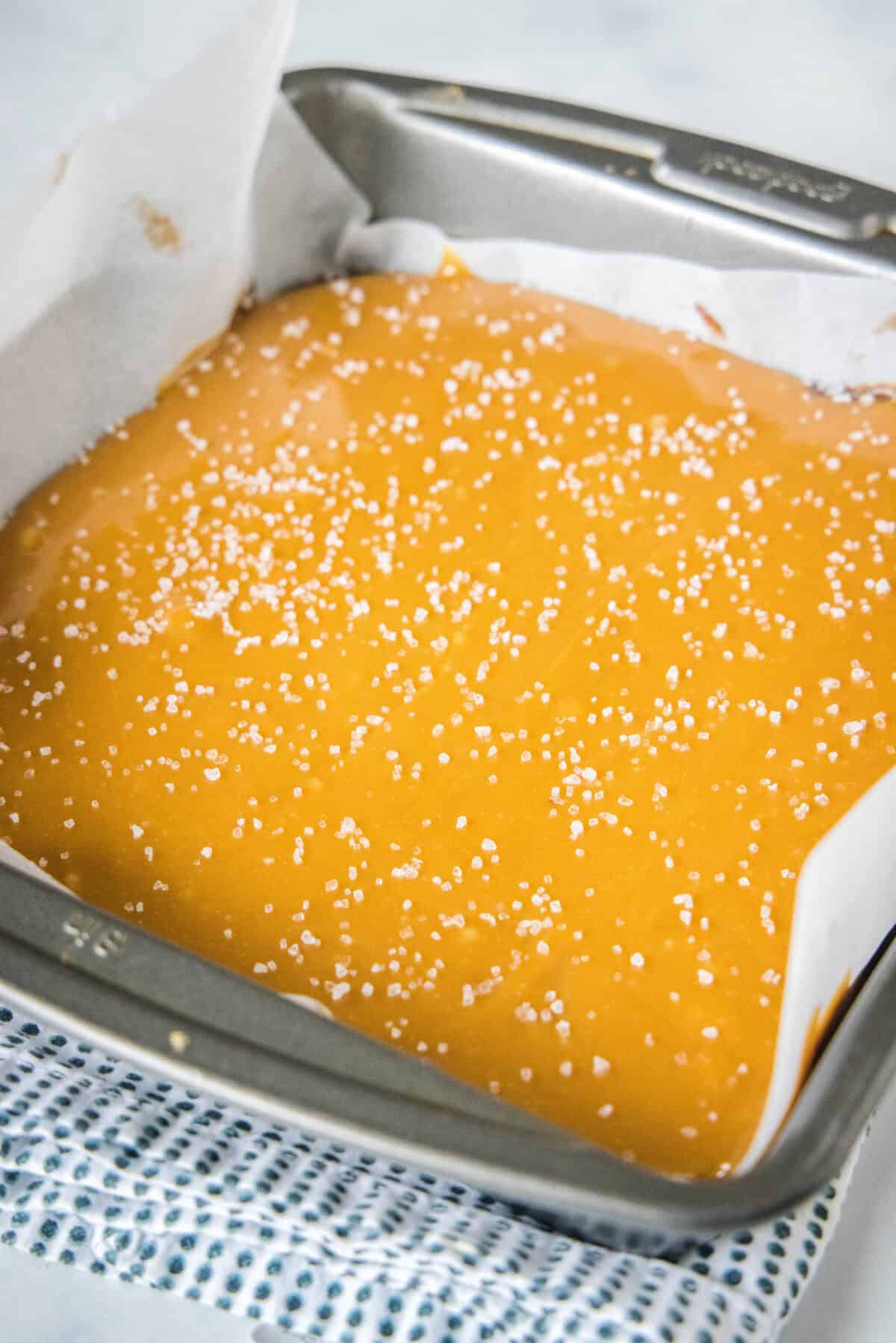 Brownie batter covered with a salted caramel layer in a lined square pan.