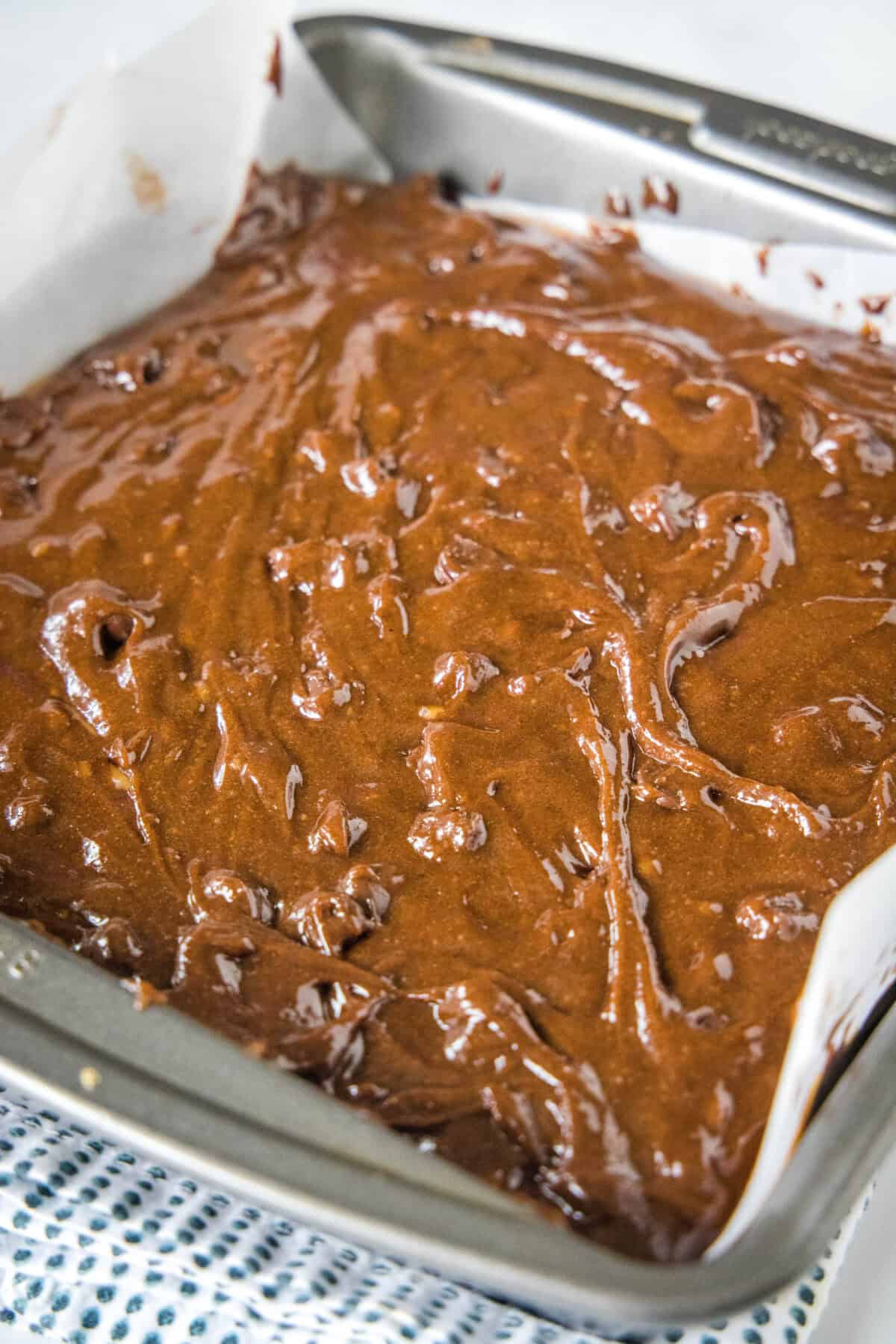 Brownie batter in a lined square baking pan.