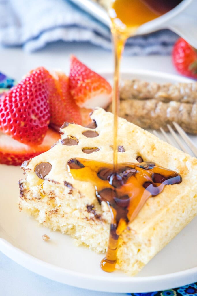 pouring syrup on a slice of pancake on a white plate