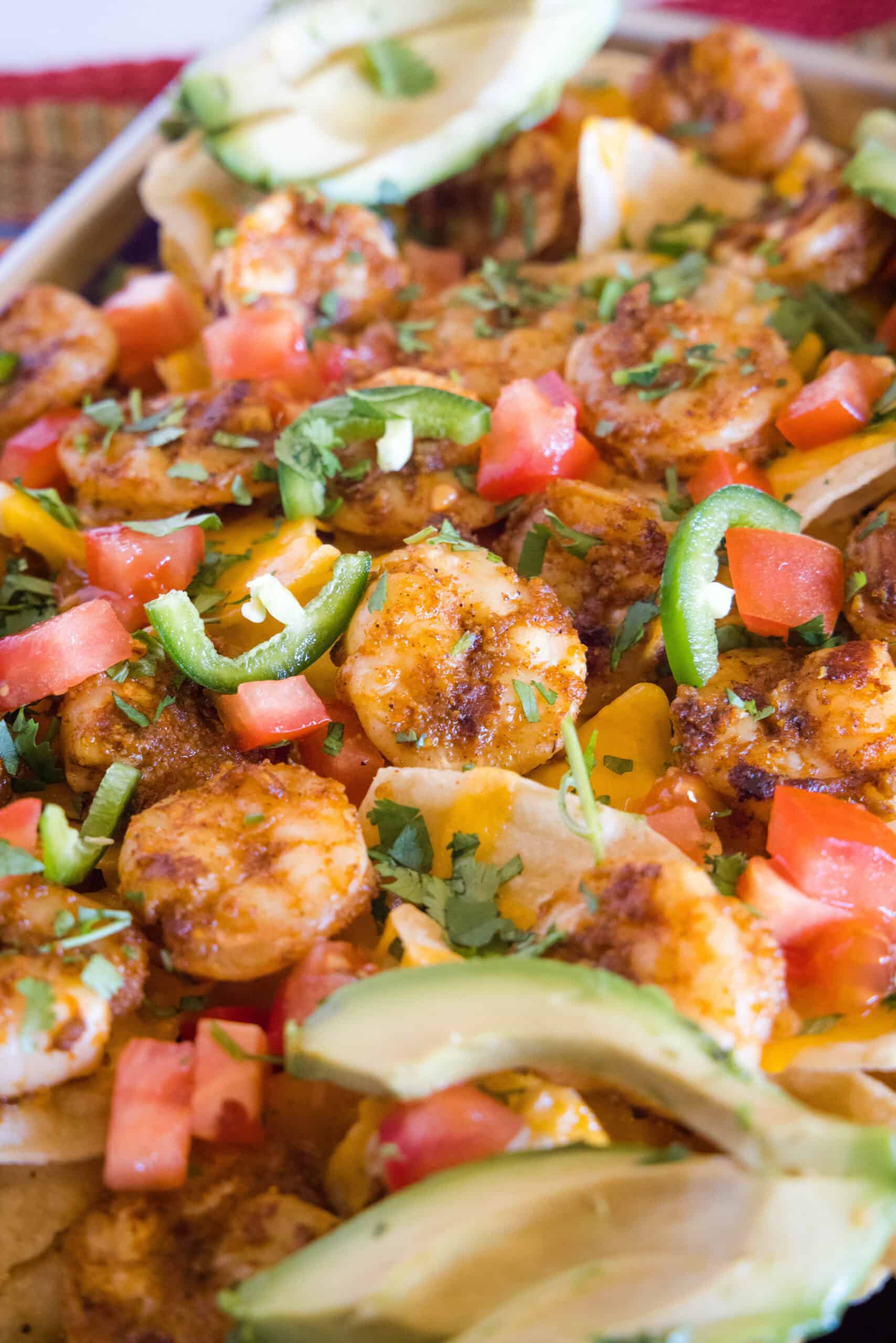 Close up of shrimp nachos on a sheet pan garnished with avocado slices.