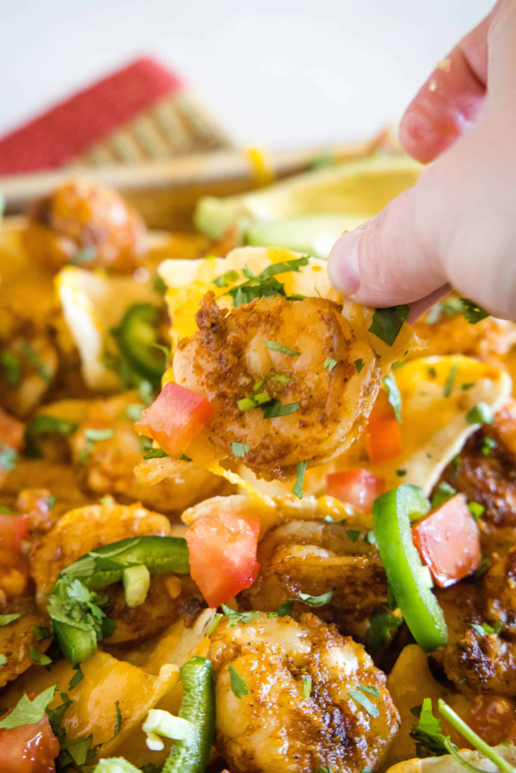 A hand lifting a nacho chip from a pan of shrimp nachos.