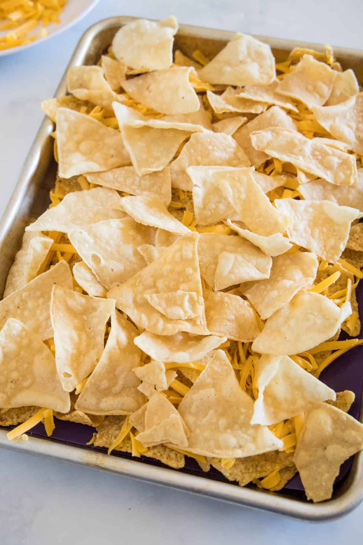 Tortilla chips layered with shredded cheese on a sheet pan.