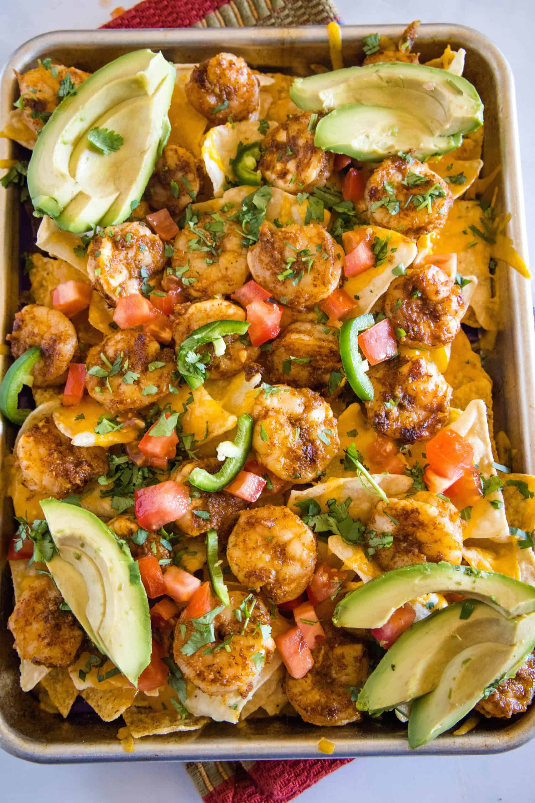 Upgrade classic nachos with zesty seasoned shrimp! These shrimp nachos are an easy Tex-Mex appetizer packed with flavor, ready in 15 minutes. Overhead view of shrimp nachos on a sheet pan garnished with avocado slices.