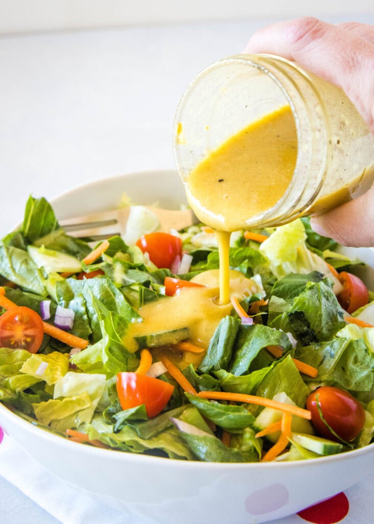 pouring dijon vinaigrette over a salad