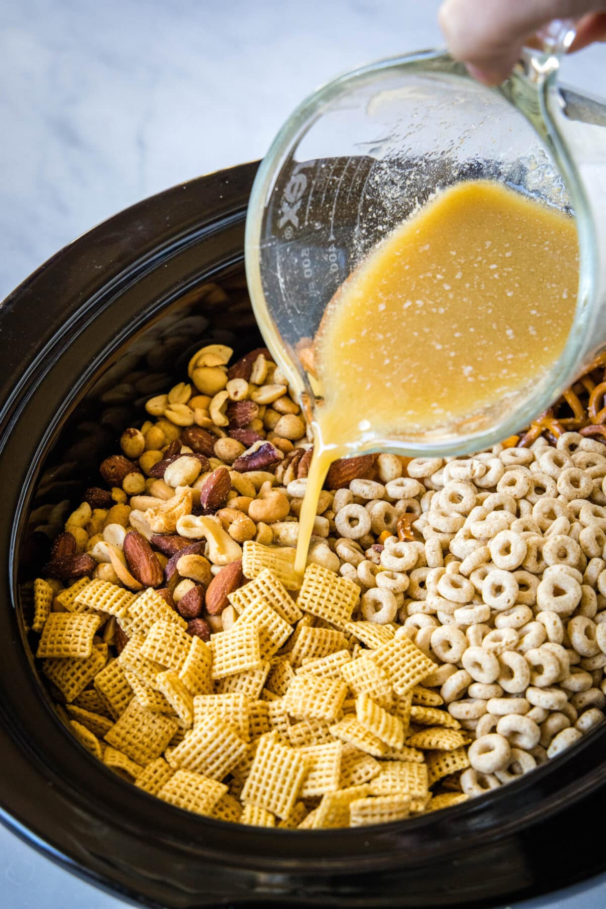 pouring butter mixture over chex mix in crock pot