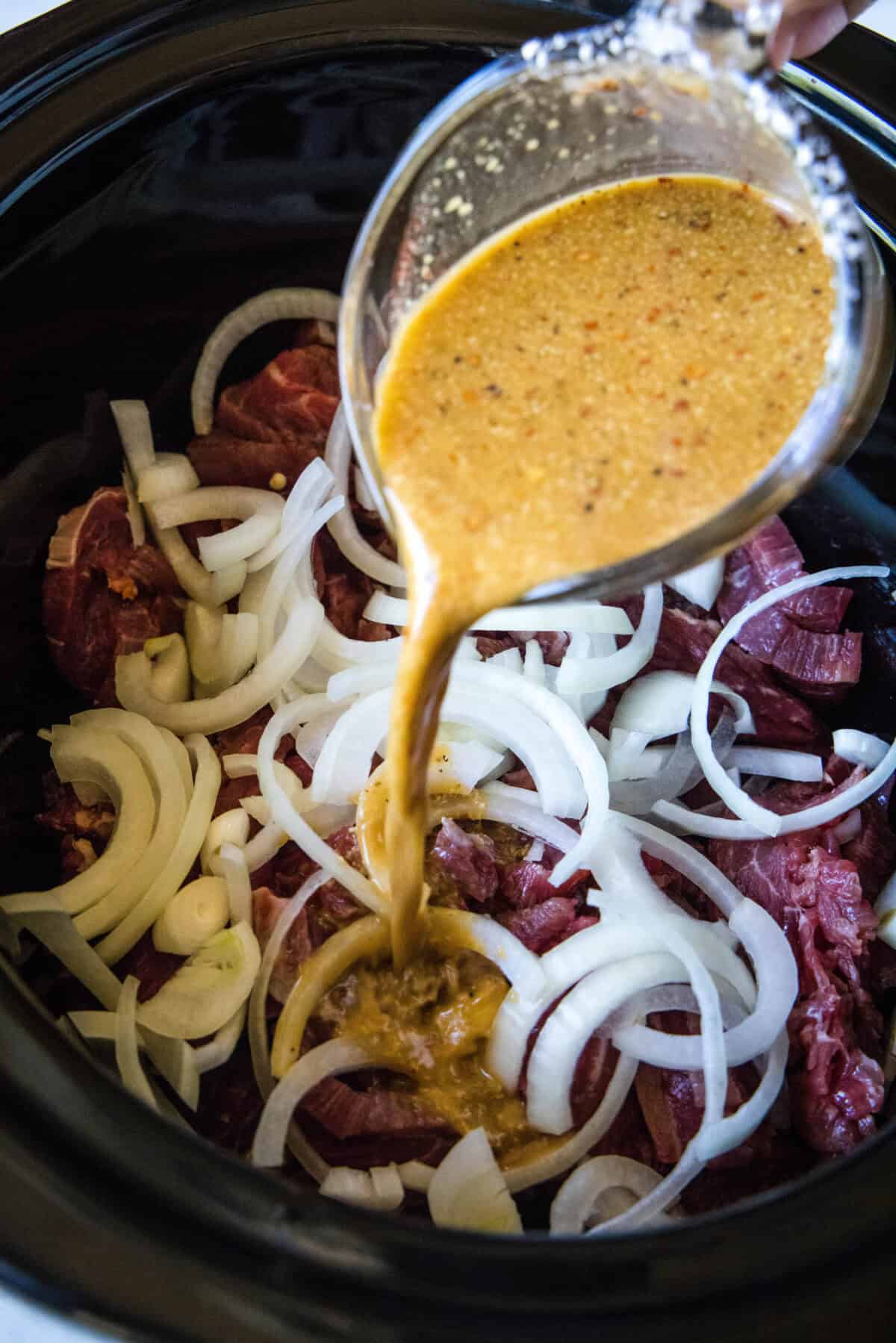 pouring sauce mixture over steak and onions