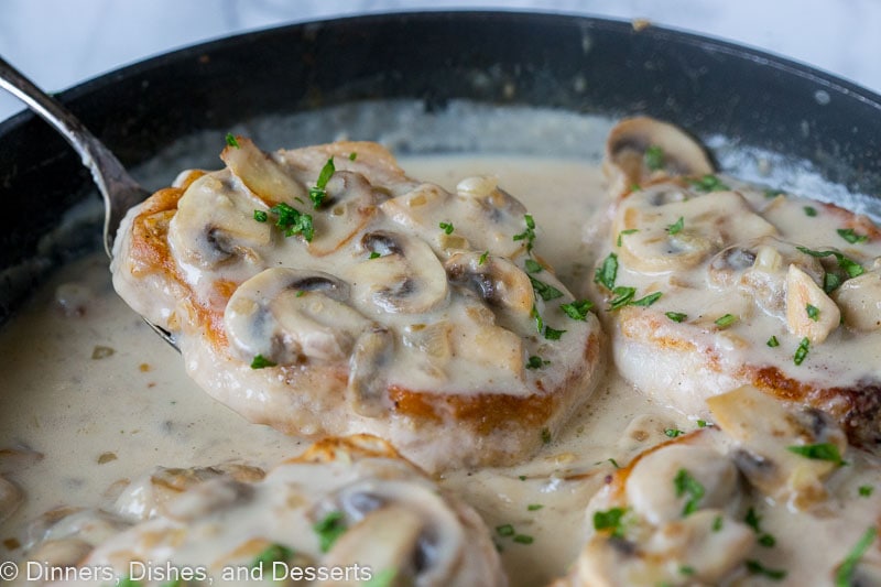 Close up of a spatula sliding under smothered pork chops with mushroom gravy in a skillet.