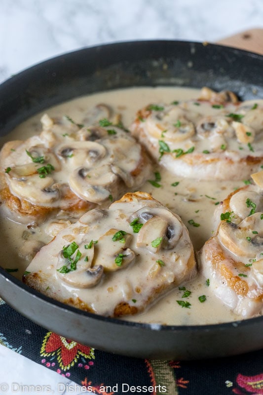 Smothered pork chops with mushroom gravy in a skillet.