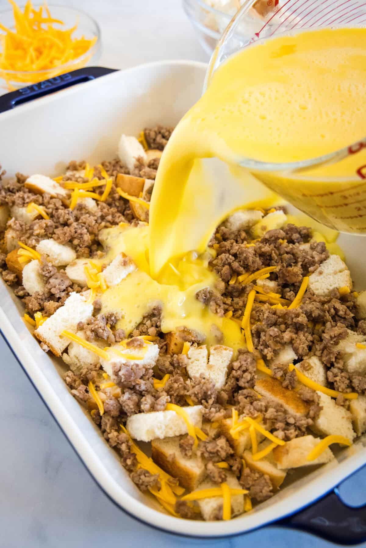 Egg mixture being poured over breakfast casserole ingredients in a baking dish.