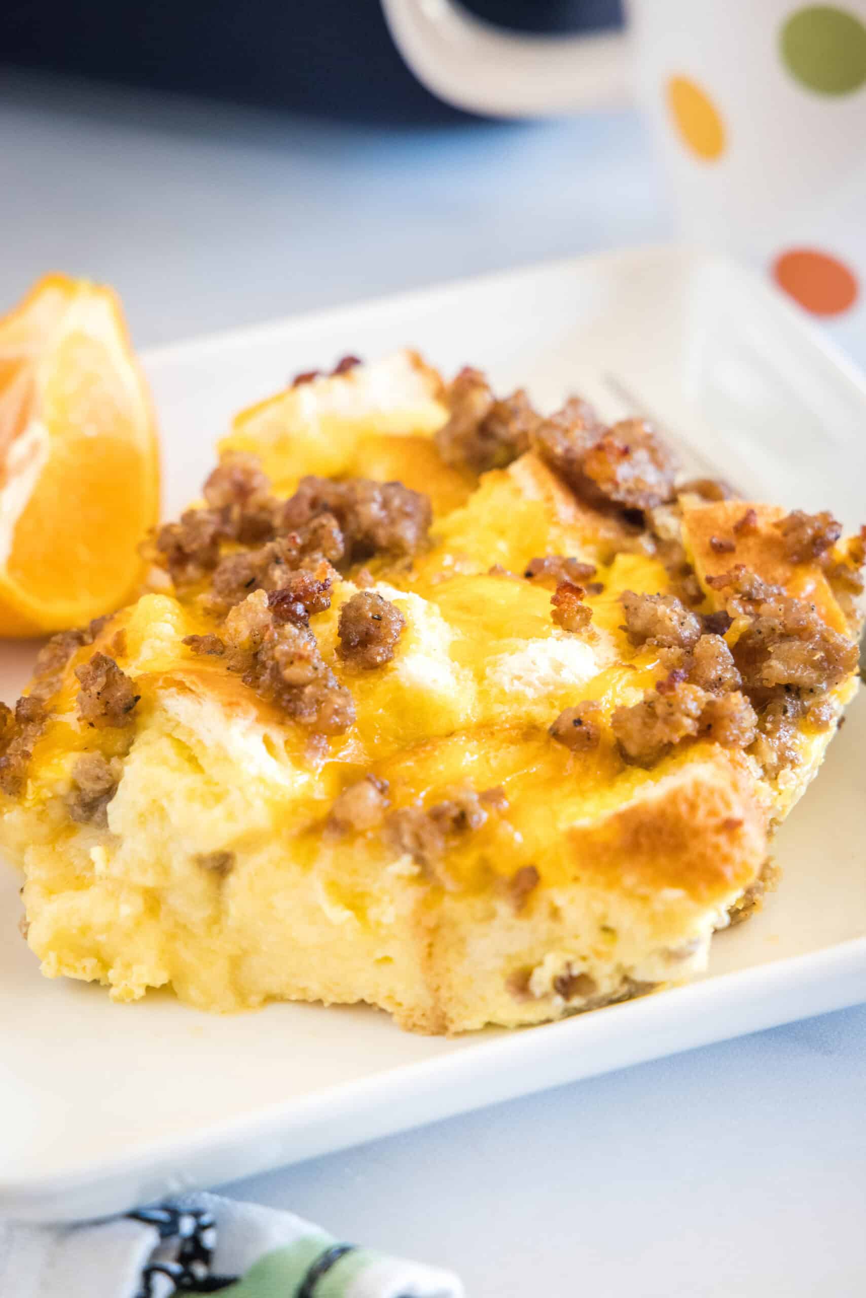 This sourdough breakfast casserole is the ultimate make-ahead breakfast packed with sourdough bread chunks, breakfast sausage, and cheese! A serving of sourdough breakfast casserole next to orange slices and a fork on a white square plate.