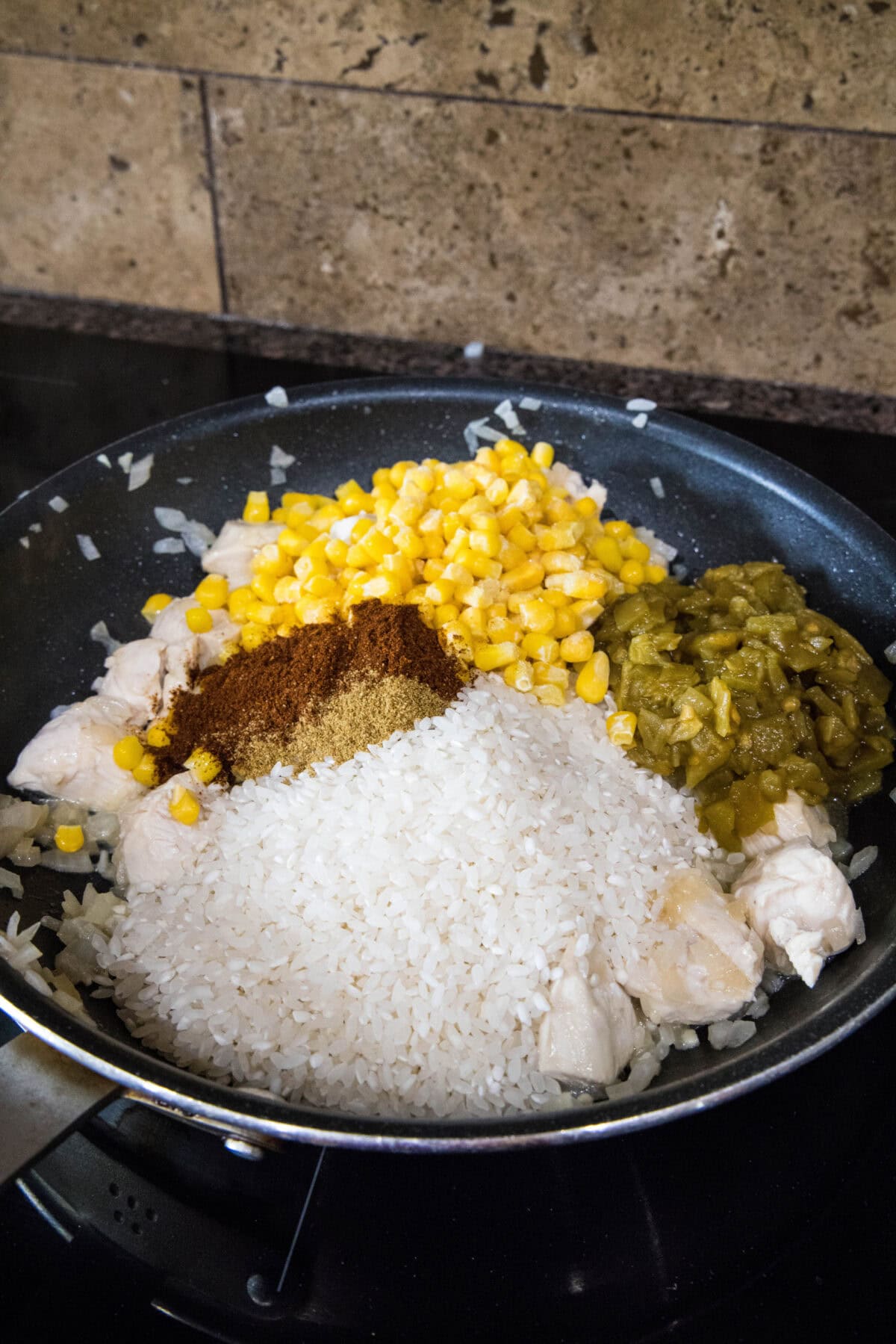 adding rice, corn, green chiles and spices to skillet with cooking chicken