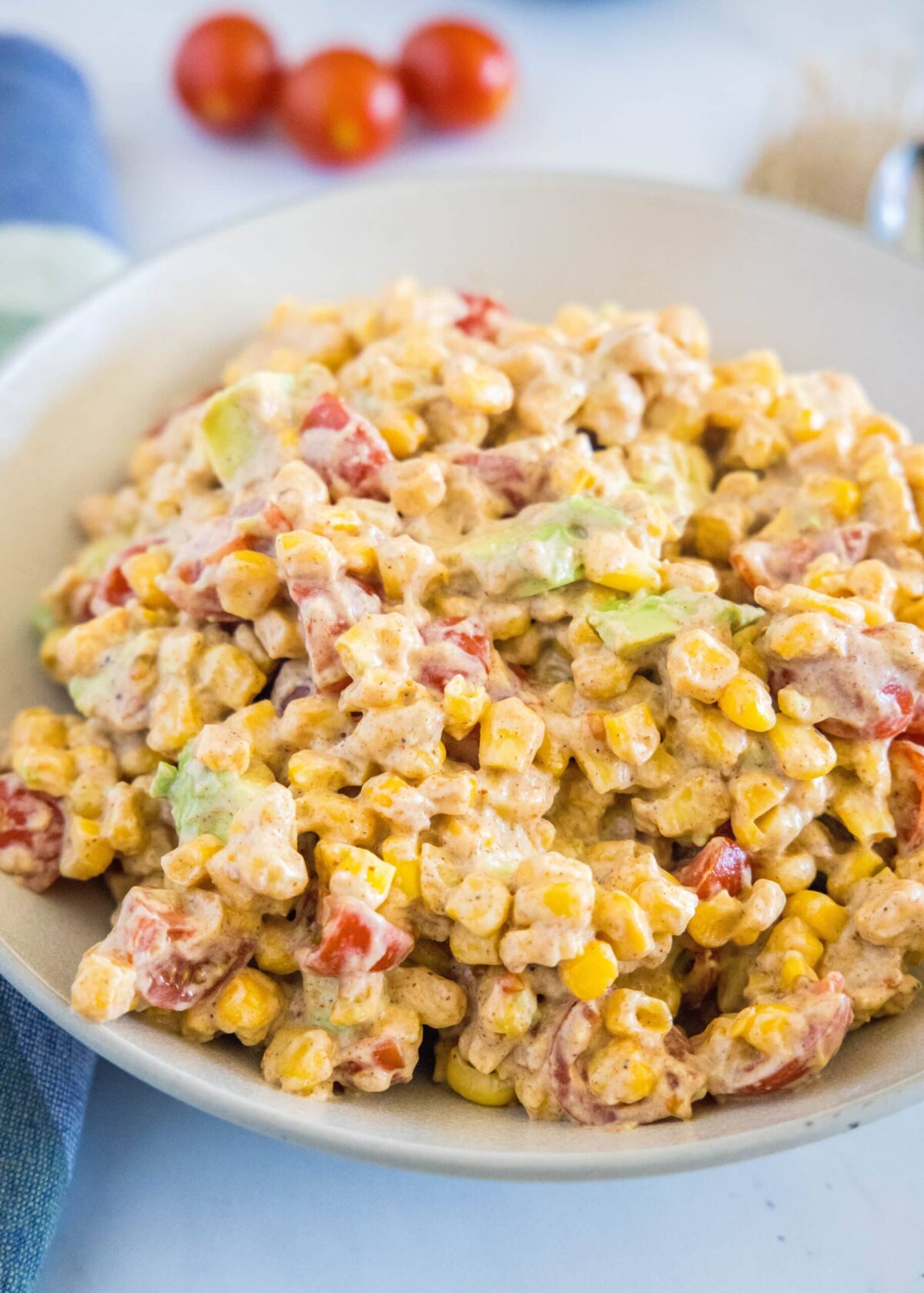 Close up of a bowl of corn salad with cherry tomatoes in the background