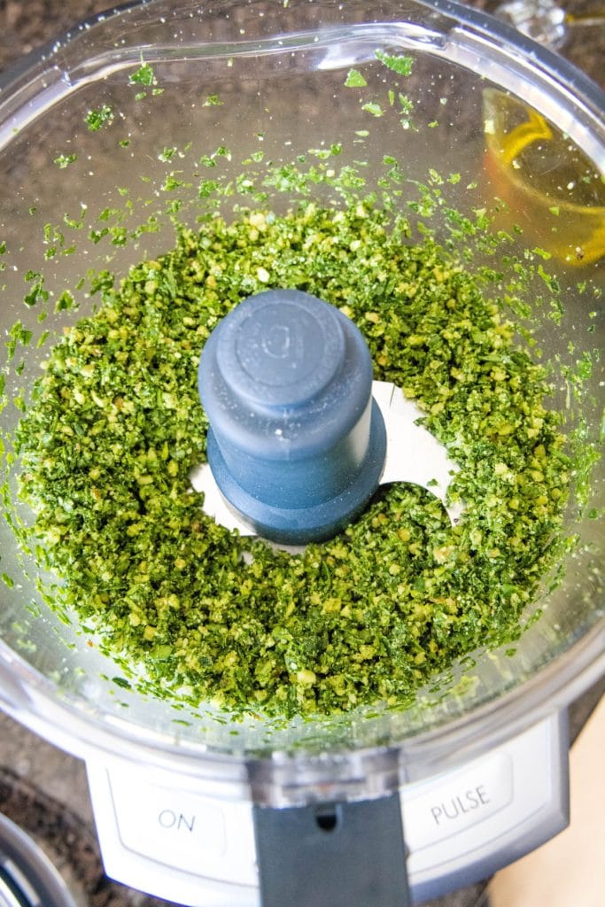 Overhead view of spinach, basil, garlic, and parmesan cheese chopped up in a food processor