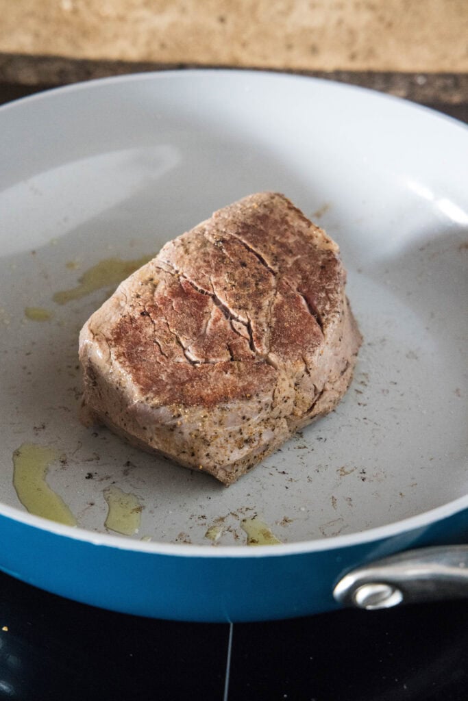 A piece of steak searing in a skillet.