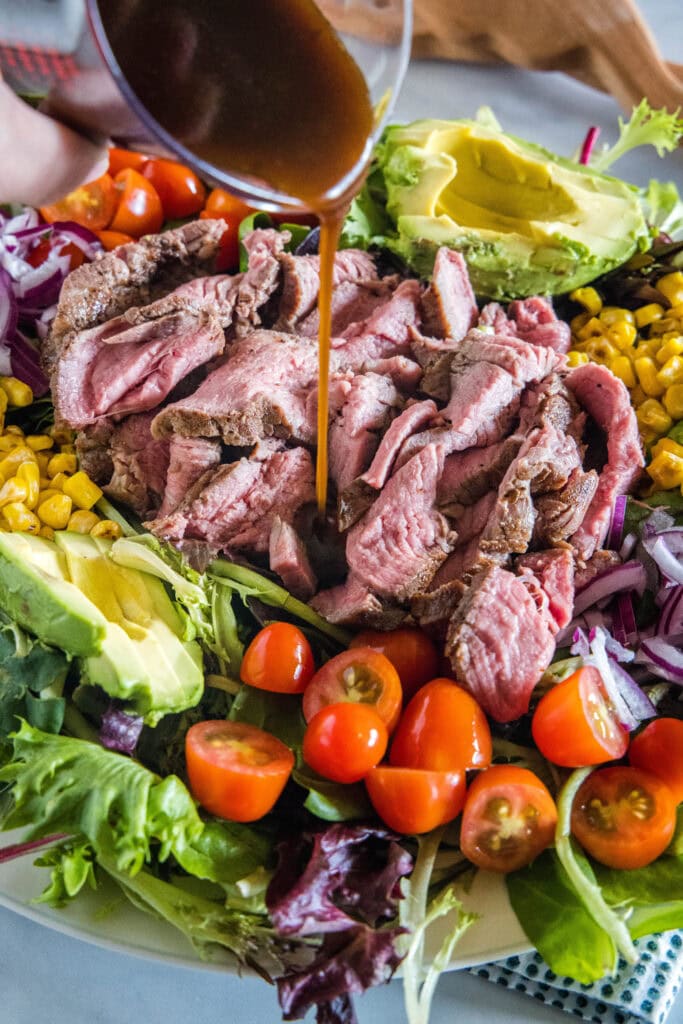 Dressing is drizzled over a large platter of steak salad.