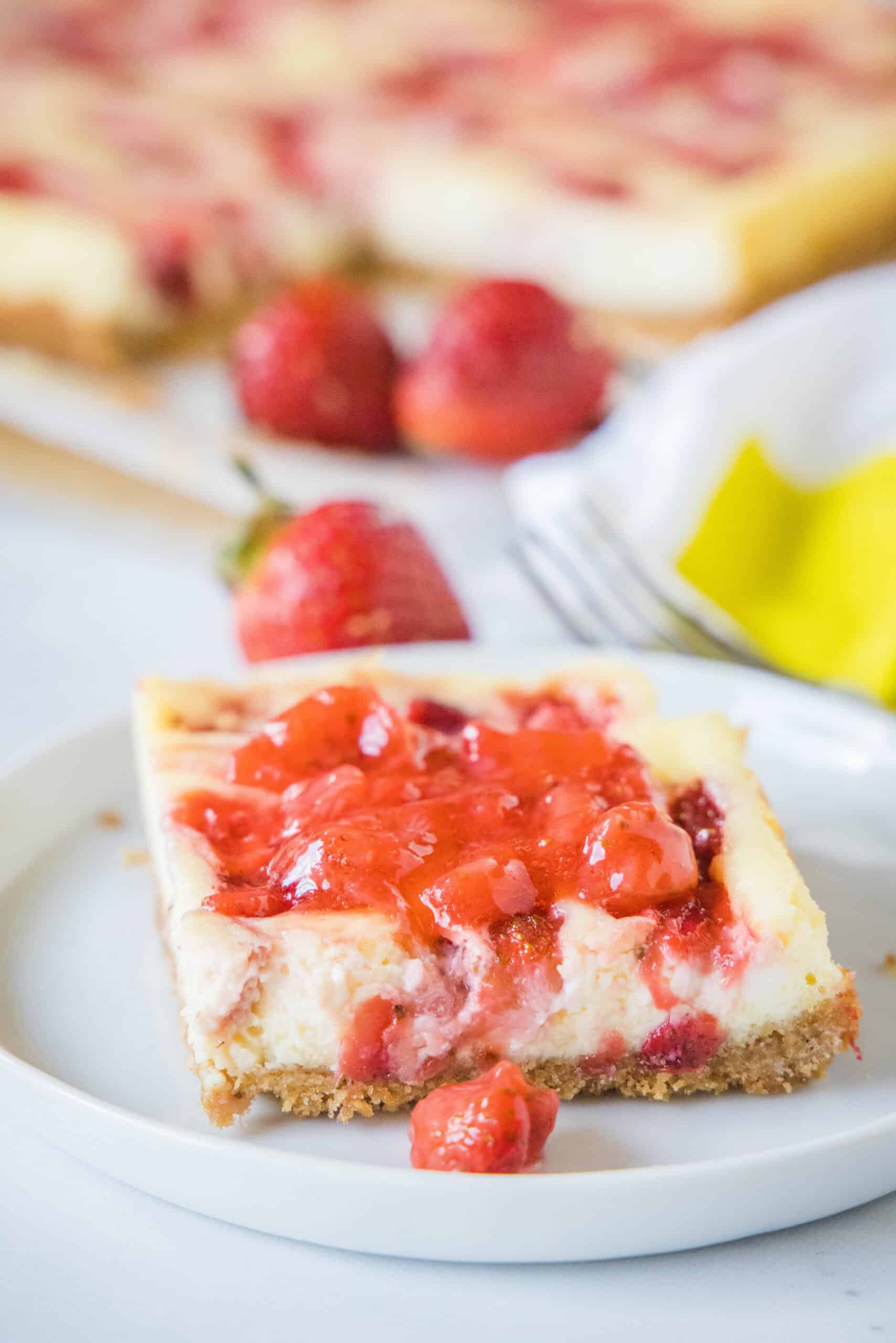 A strawberry cheesecake bar topped with strawberry compote on a plate.