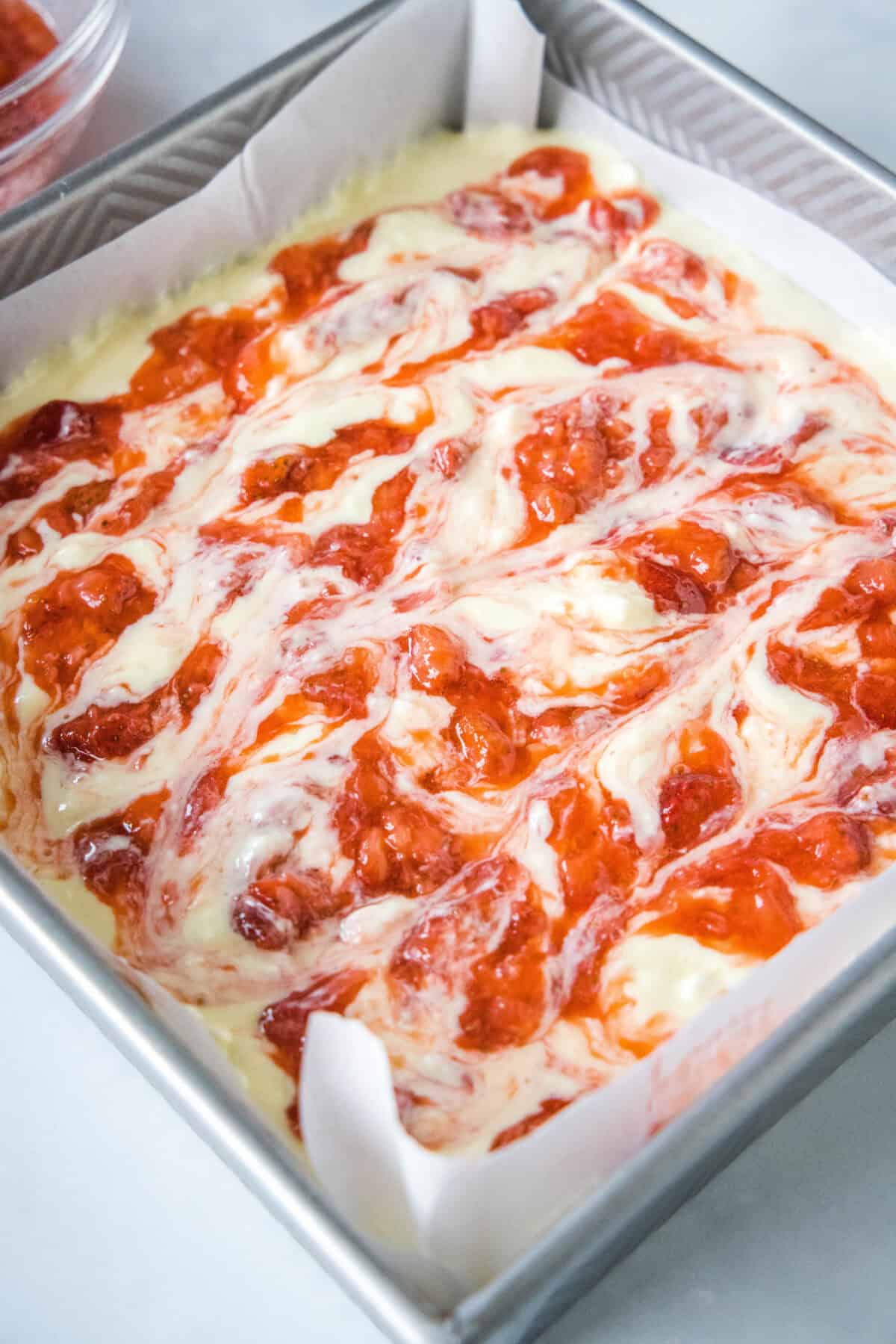 Unbaked strawberry cheesecake bars assembled in a baking dish.
