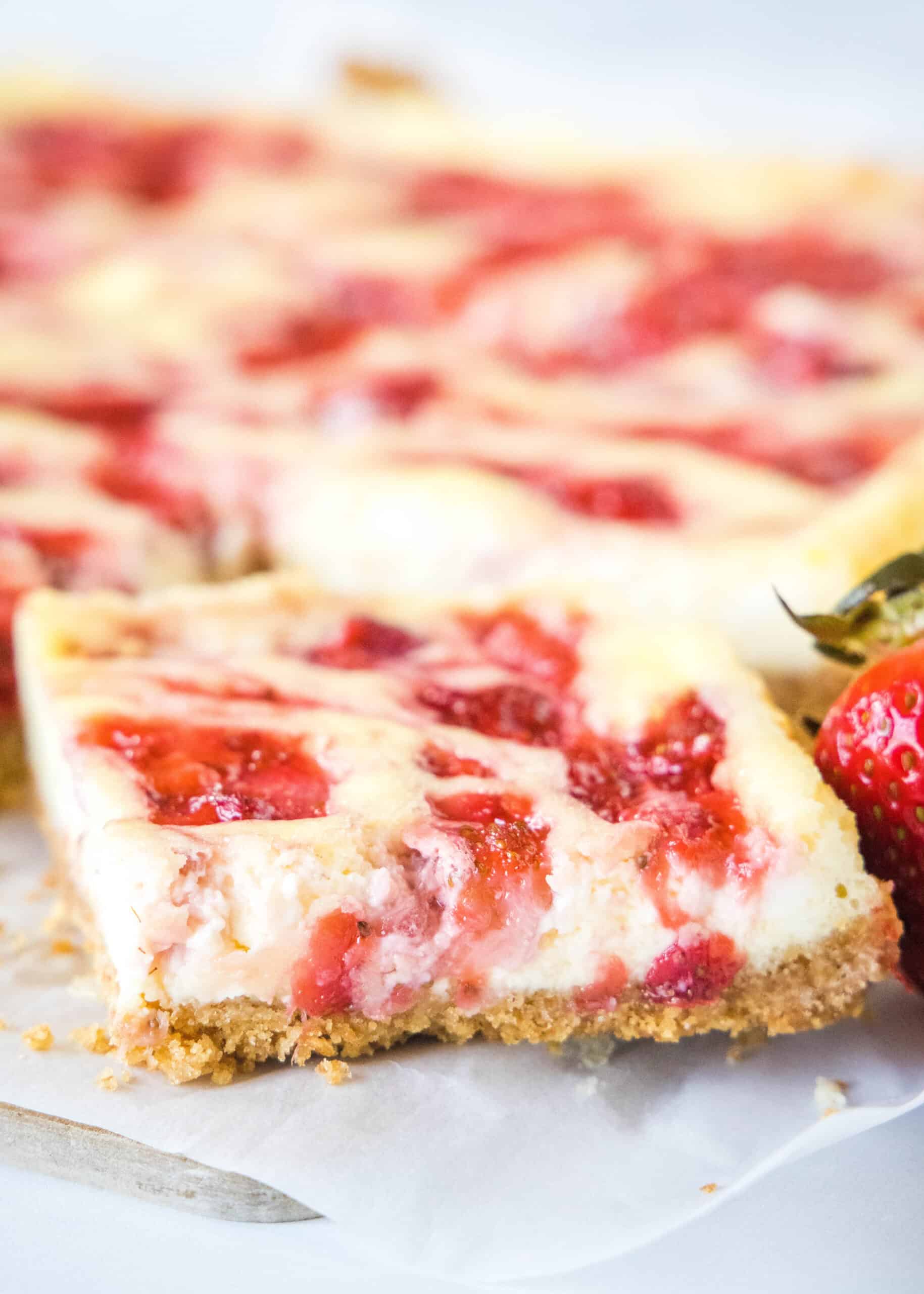 Close up of a strawberry cheesecake bar with more bars in the background.