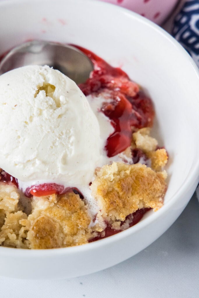 strawberry dump cake in a bowl topped with ice cream