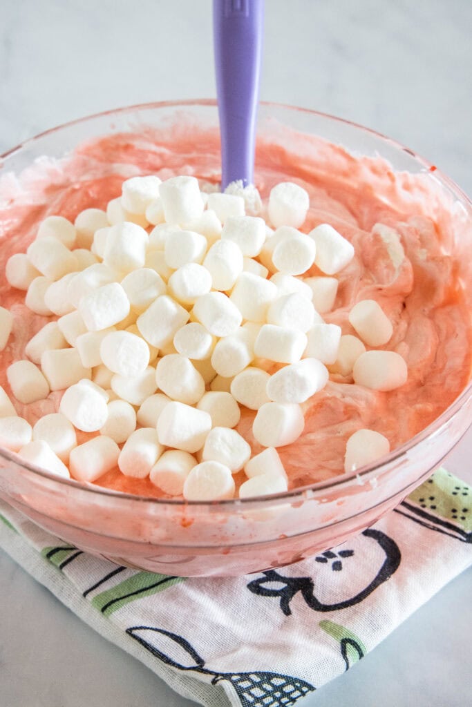 Mini marshmallows added to a bowl of strawberry fluff ingredients.