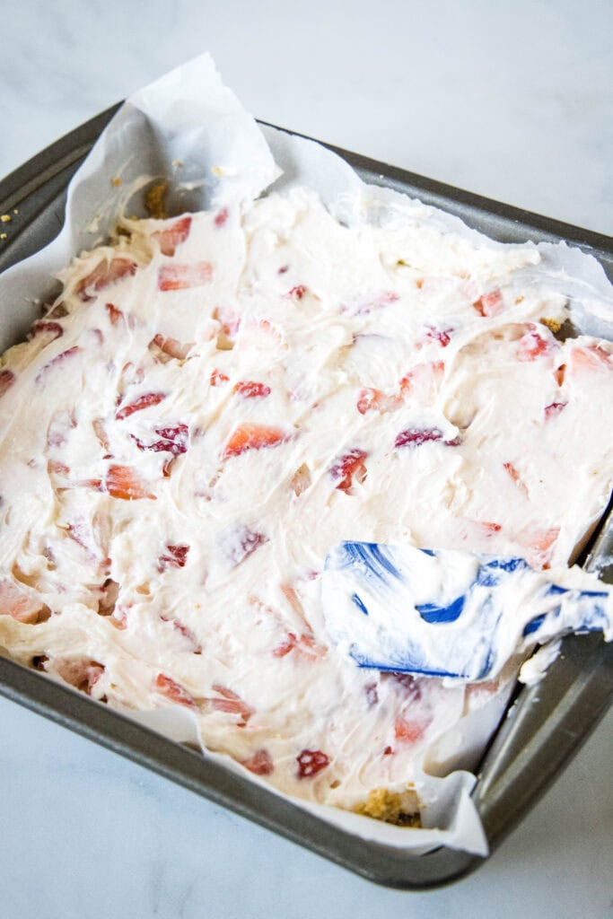 spreading cream cheese and strawberry layer into a baking dish